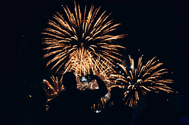 Homme de dos qui prend en photo des feux d'artifice sur son cellulaire