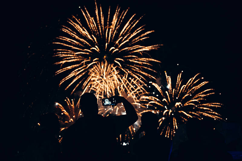 Man from behind taking pictures of fireworks on his cell phone